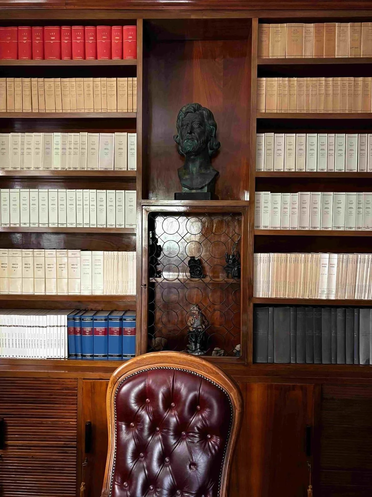 La biblioteca storica dello Studio Legale Sassano, con i volumi giuridici, il busto in bronzo e la poltrona in pelle.